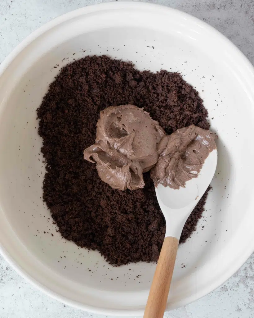 A large mixing bowl containing chocolate cake crumbs and chocolate raspberry buttercream, about to be mixed together.