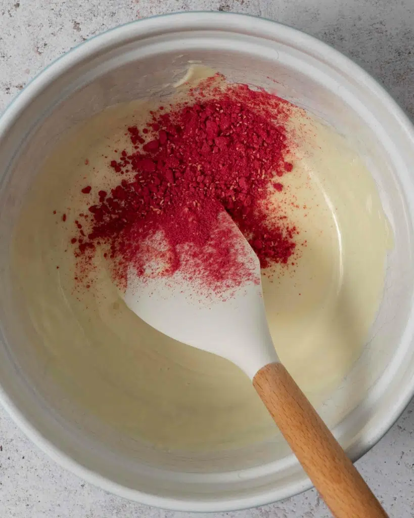 A bowl of melted white chocolate and freeze dried raspberry powder.
