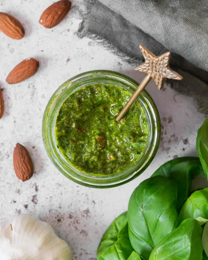 An photograph of an open jar of almond pesto (vegan) with a gold star spoon poking out