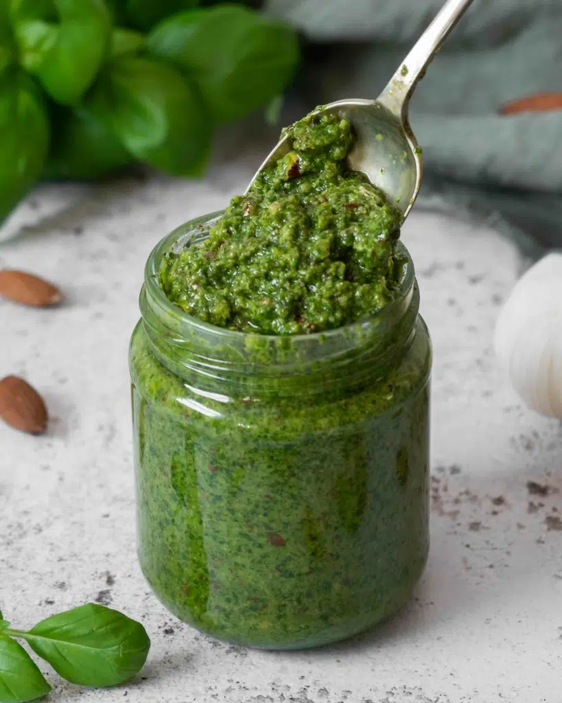 A jar of almond pesto (vegan) with a spoonful of vibrant green pesto being lifted out