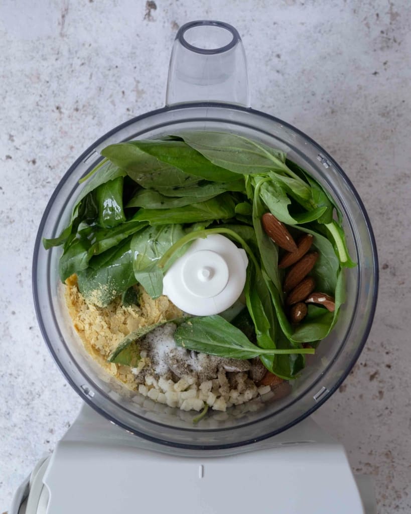 A food processor full of the (unblended) ingredients needed to make fresh almond pesto (vegan)