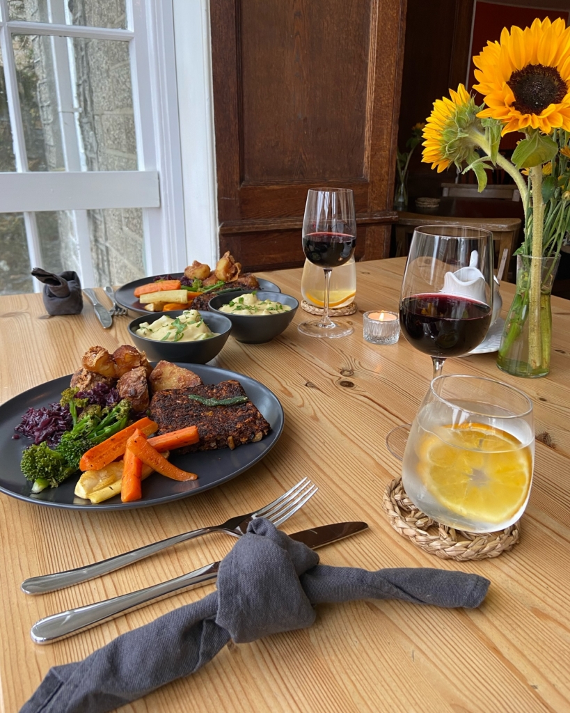 Two vegan Sunday roast dinners on a wooden table with red wine and sunflowers