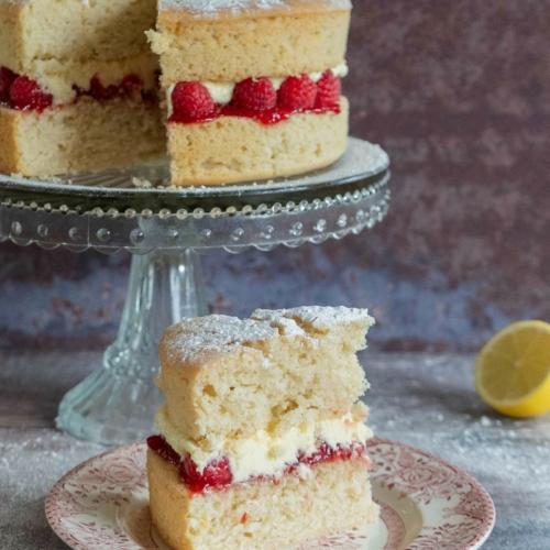 A slice of vegan lemon and raspberry cake on a pretty vintage plate