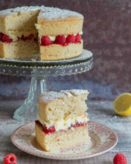 A slice of vegan lemon and raspberry cake on a pretty vintage plate