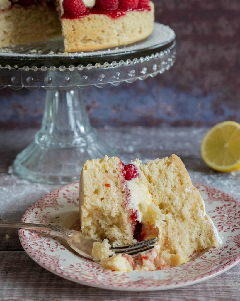 A slice of tender vegan lemon and raspberry cake on a plate with a forkful taken out of it