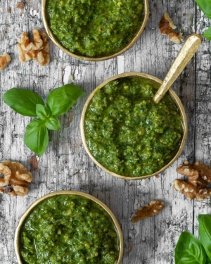 Close up overhead photograph of a small bowl of vegan walnut pesto, surrounded by raw walnuts and fresh basil leaves