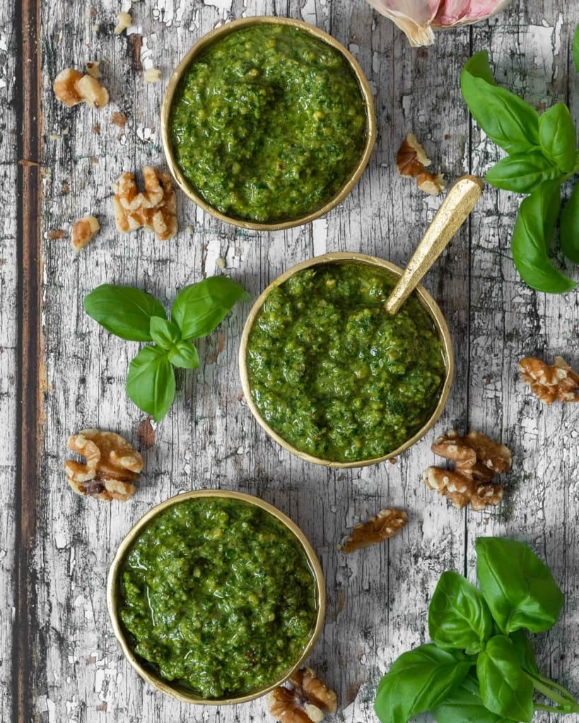 An overhead photograph of vegan basil walnut pesto in three small gold bowls