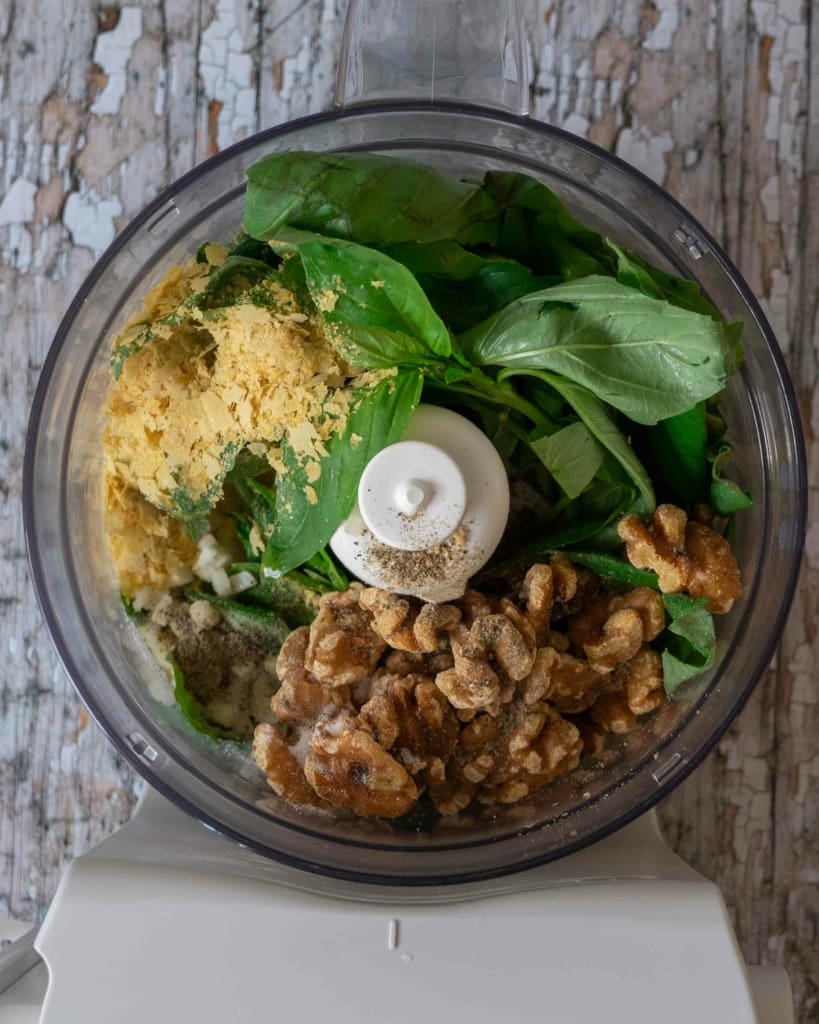 A food processor filled with the ingredients needed to make walnut pesto