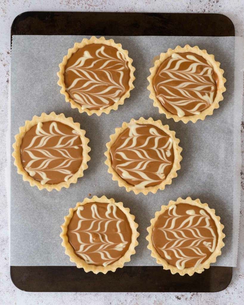 Biscoff tarts decorated with melted white chocolate marbling, ready to go into the fridge to set