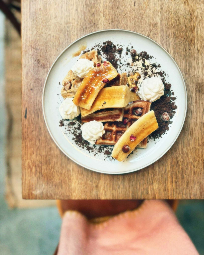 Vegan waffles on a white plate with caramelised slices of banana and whipped cream