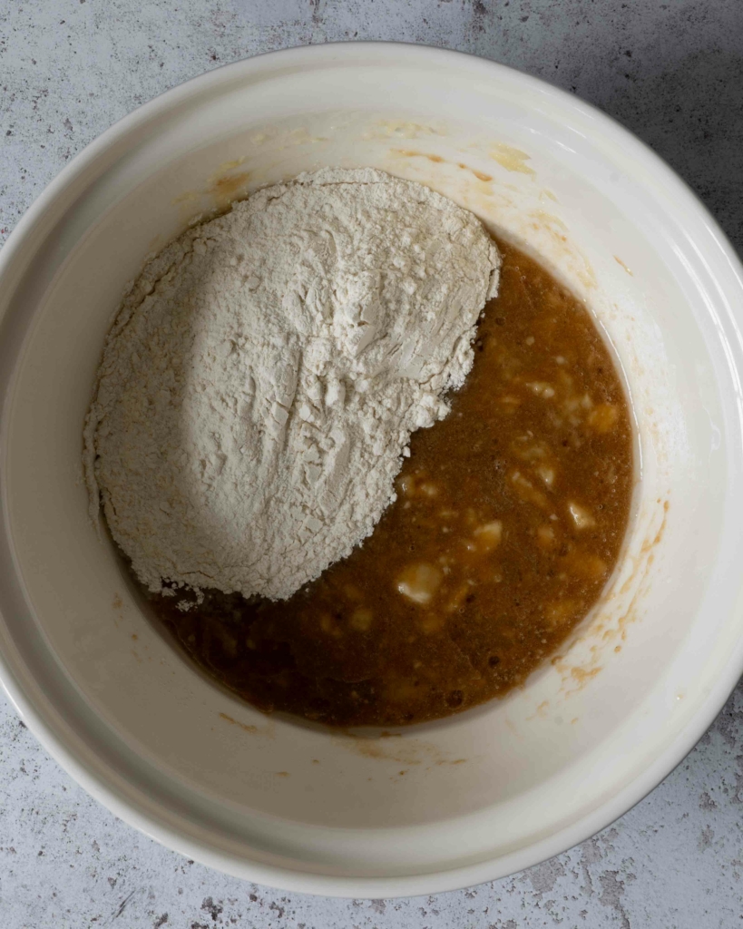 Flour added to a bowl of wet ingredients for making vegan banana bread