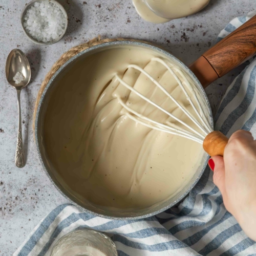 Thick and creamy vegan bechamel sauce in a saucepan being whisked