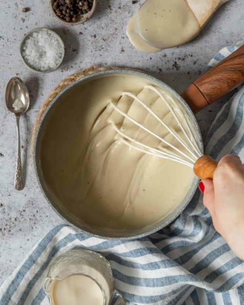 Thick and creamy vegan bechamel sauce in a saucepan being whisked