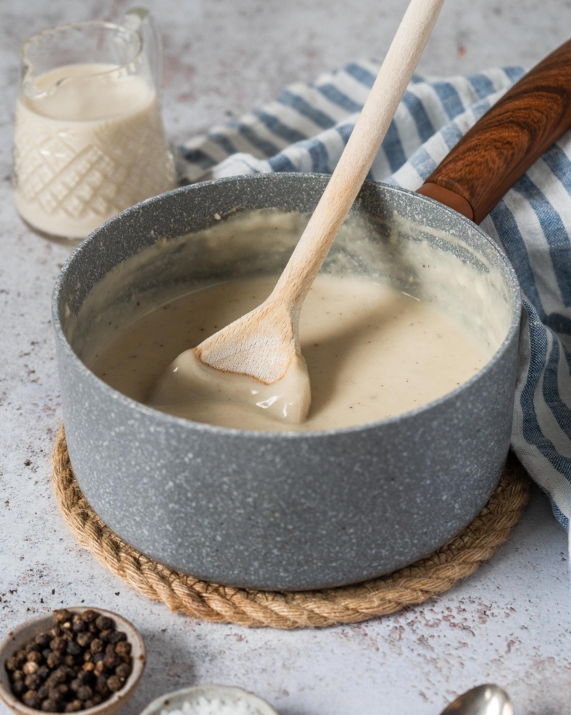 Vegan white sauce in a saucepan with a wooden spoon stirring the sauce