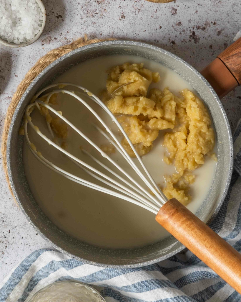 Roux and oat milk in a saucepan about to be whisked together