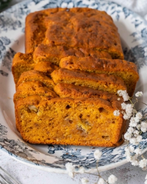 A vibrant, colourful and moist vegan banana pumpkin bread on a pretty blue floral plate, cut into slices.
