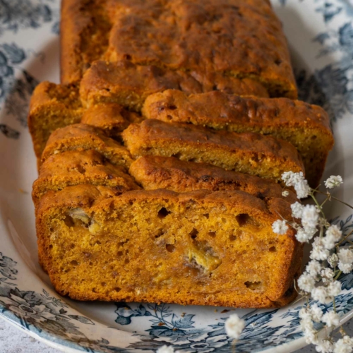 A vibrant, colourful and moist vegan pumpkin banana bread on a pretty blue floral plate, cut into slices.