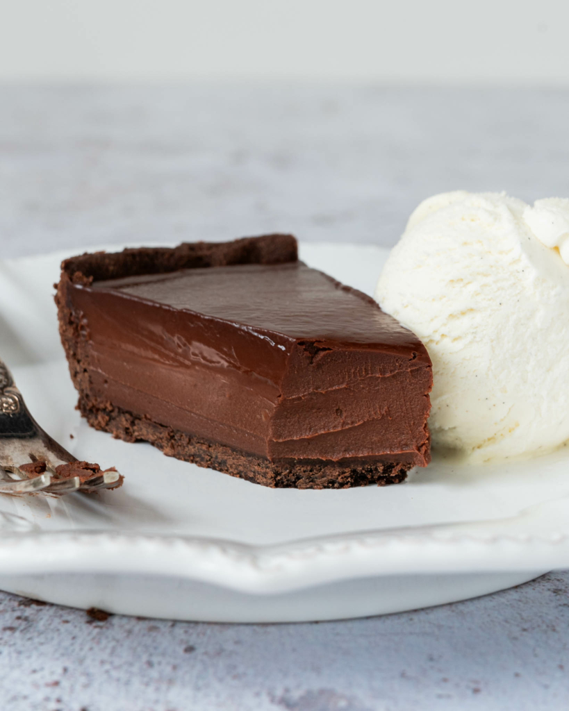 A piece of French Chocolate Tart on a white plate with a forkful missing