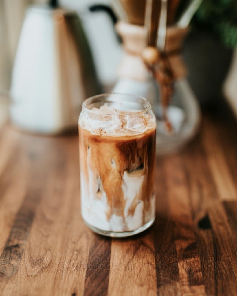 A glass of oat milk iced coffee on a wooden bench