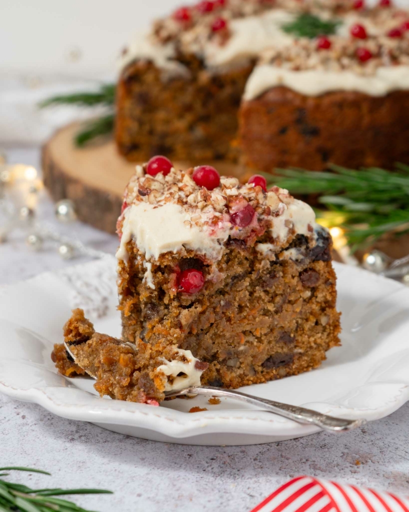 A slice of Christmas carrot cake on a white plate with a fork resting on the side