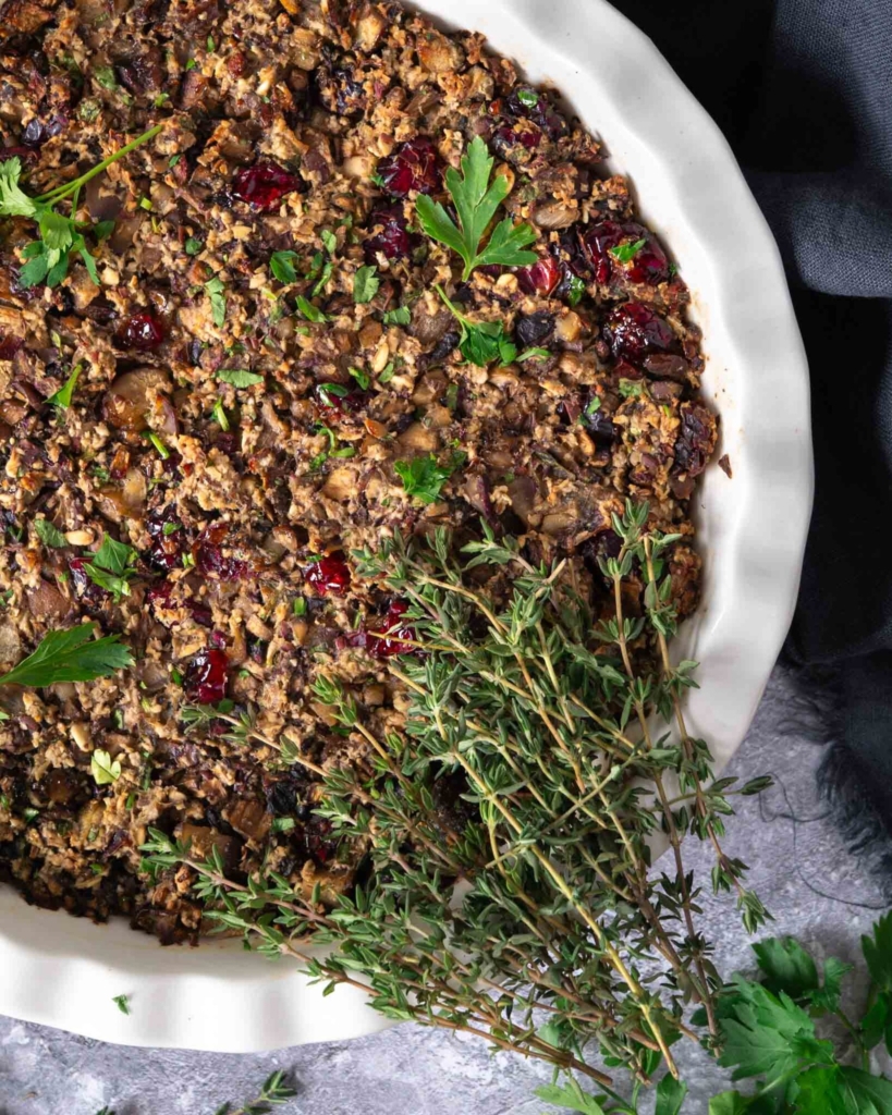 A dish of vegan chestnut stuffing studded with juicy cranberries and sprinkled with fresh herbs