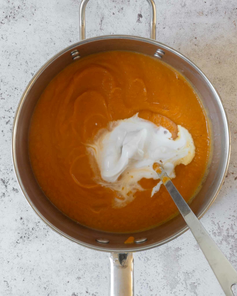 Sweet potato soup in a saucepan with a dollop of coconut cream on top