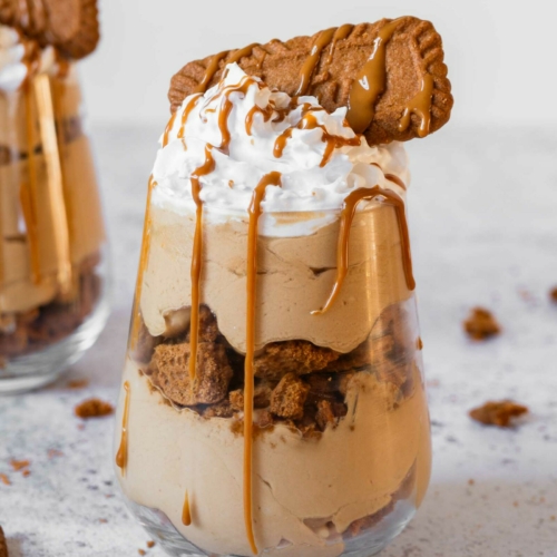 A layered no bake Biscoff cheesecake cup with a creamy cheesecake filling, layers of Biscoff biscuits and whipped vegan cream on top