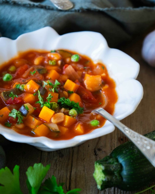 A bowl of colourful farmhouse vegetable soup on a rustic wooden farmhouse table with fresh ingredients surrounding it