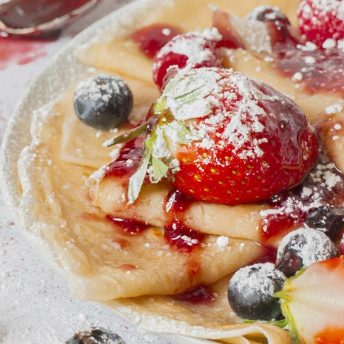 A plate of freshly cooked crepes topped with berries and icing sugar