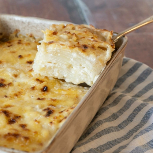 A neatly sliced portion of vegan potatoes dauphinoise being lifted out of a baking dish