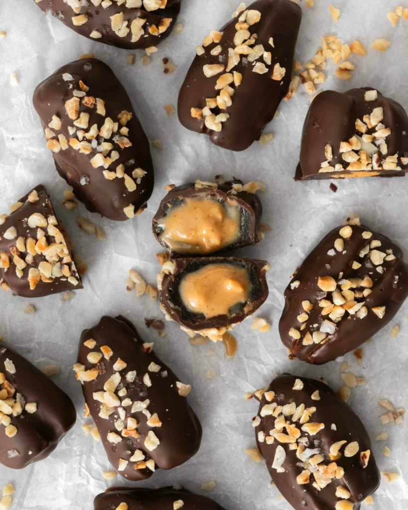 Vegan snickers dates on a tabletop, one cut open to reveal a gooey date and peanut butter inside