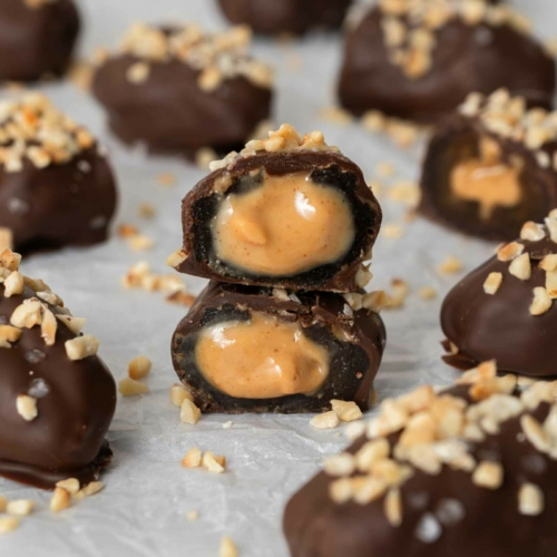 Vegan snickers dates on a tabletop, one cut open to reveal a gooey date and peanut butter inside