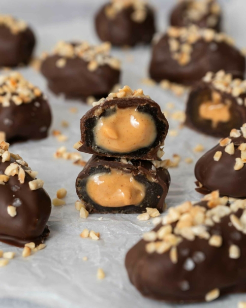 Vegan snickers dates on a tabletop, one cut open to reveal a gooey date and peanut butter inside