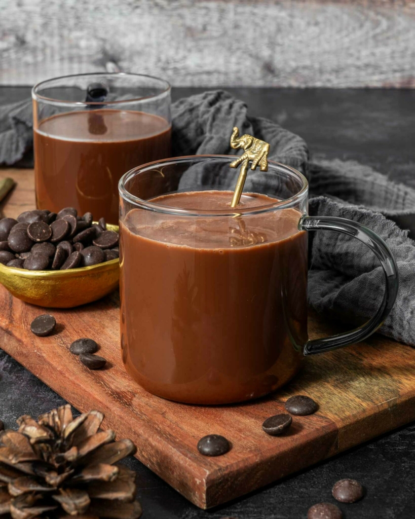 Two mugs of silky smooth hot chocolate with oat milk sat on a wooden board