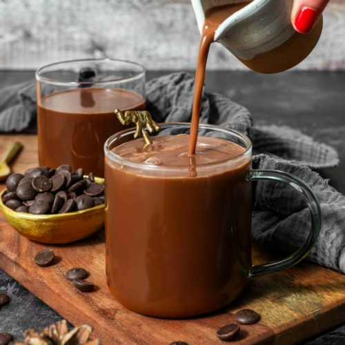 Hot chocolate with oat milk being poured from a jug into a glass cup