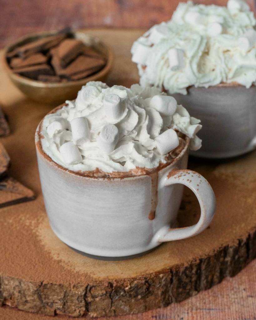 A mug of vegan hot chocolate topped with dairy free cream and vegan mini marshmallows