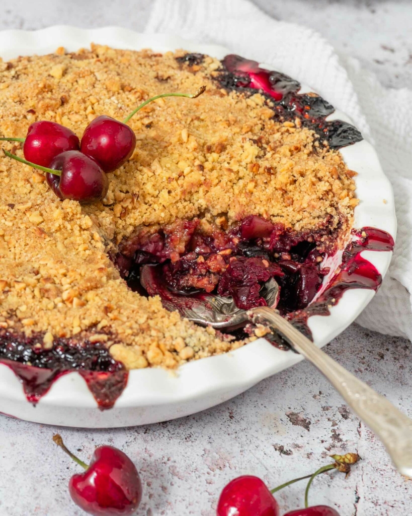 A dish of apple cherry crumble with a spoonful missing