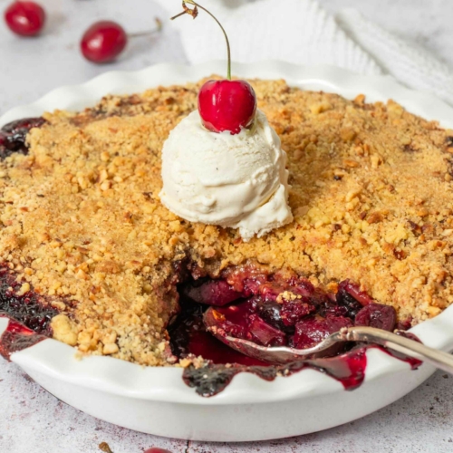 A freshly baked apple cherry crumble with vegan vanilla ice cream and a fresh red cherry on top