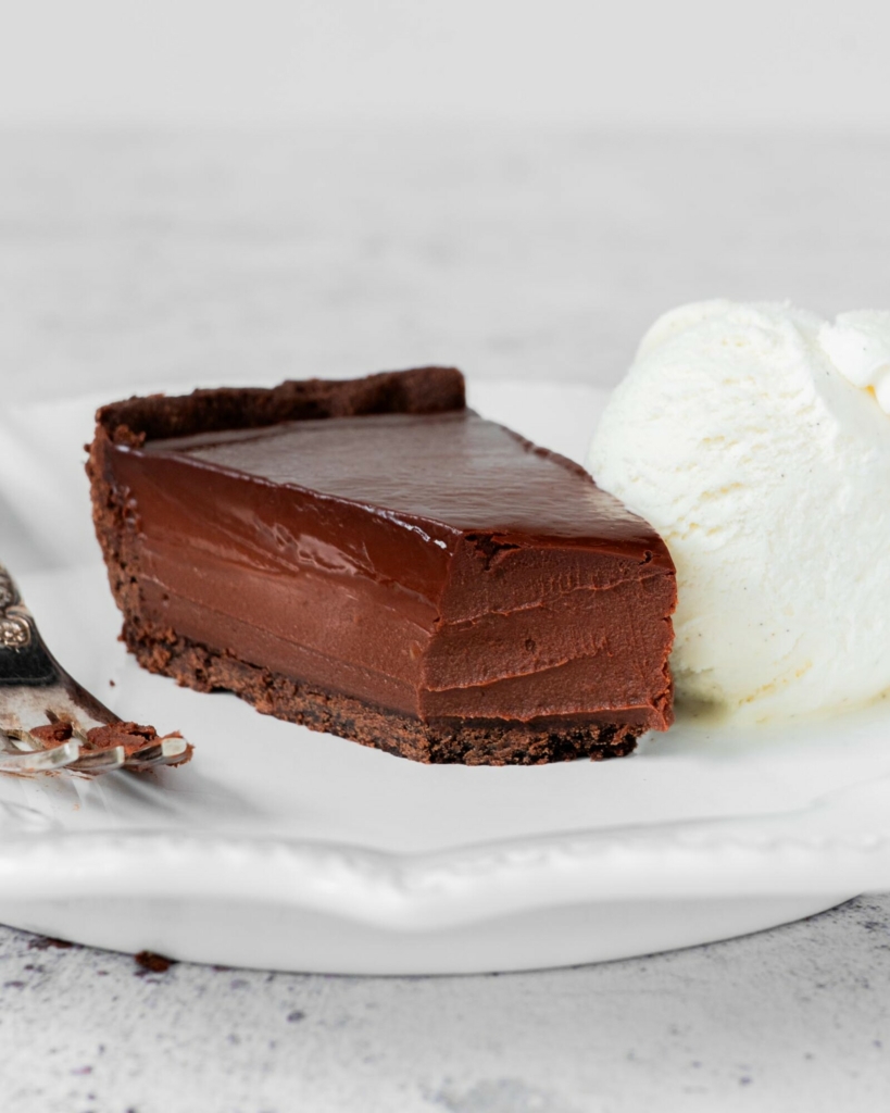 A piece of French Chocolate Tart on a white plate with a forkful missing