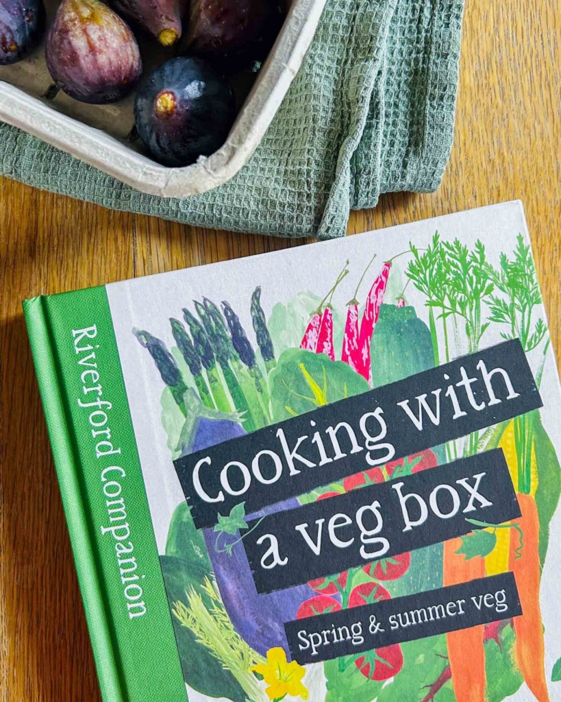 The Riverford spring summer cookbook next to a box of fresh figs, ready to review