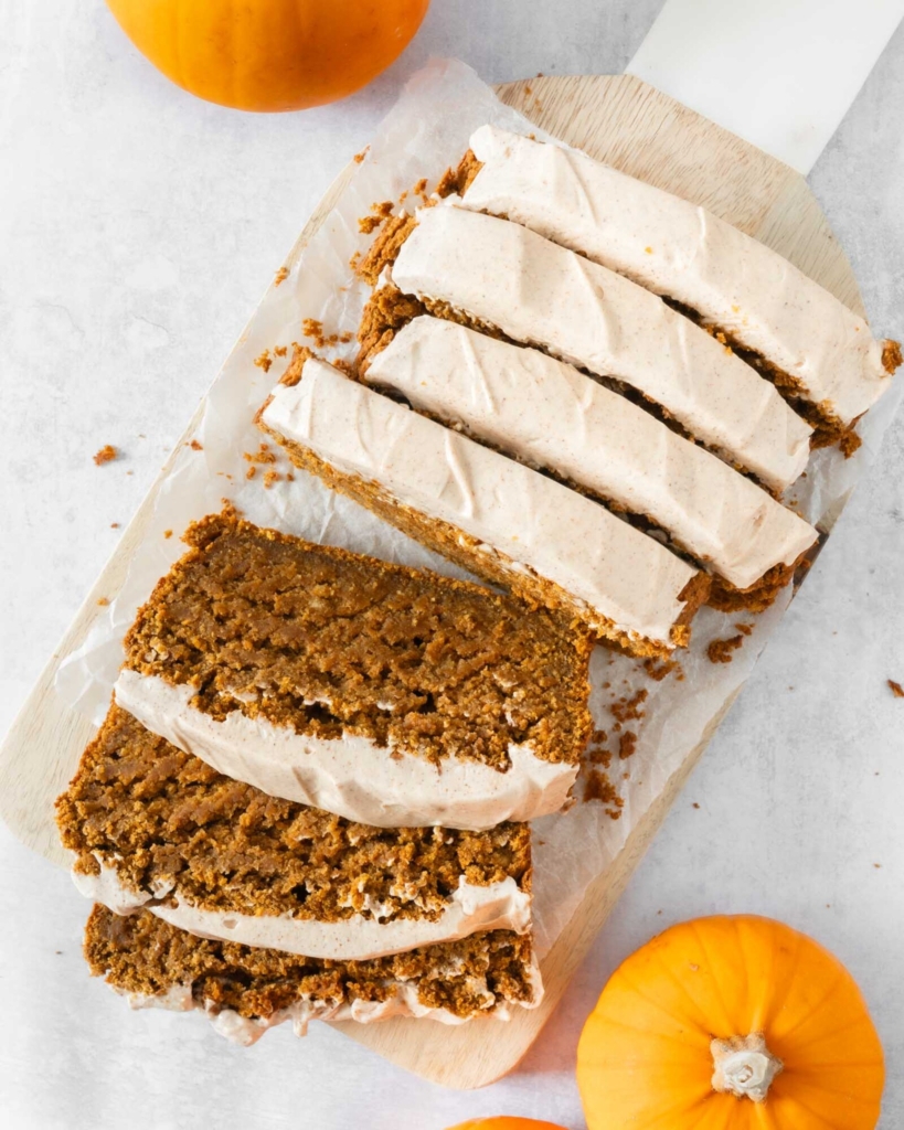 Slices of gluten free pumpkin cake on a chopping board, topped with cinnamon cream cheese