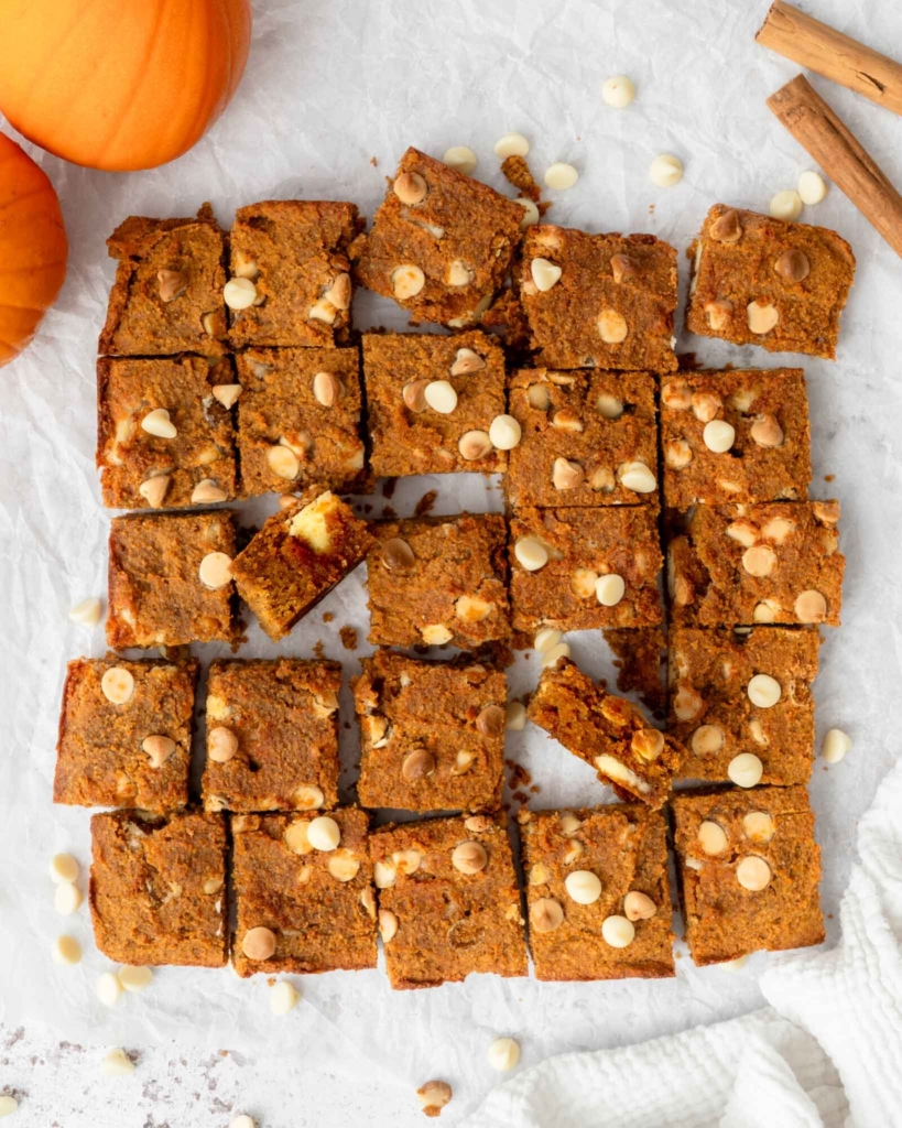 Vegan pumpkin chickpea blondies cut up into little squares on a table top, sprinkled with white chocolate chips