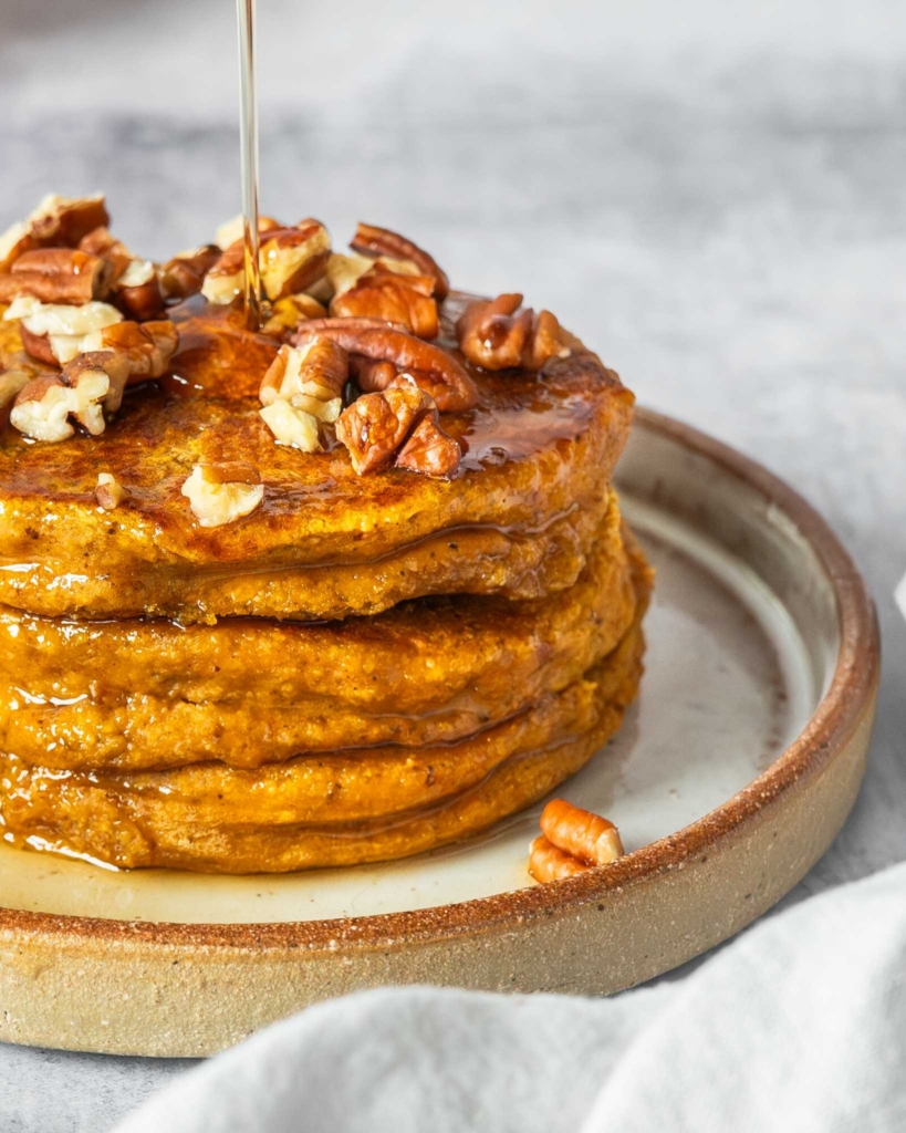 Vegan pumpkin pancakes topped with crumbled pecans and maple syrup