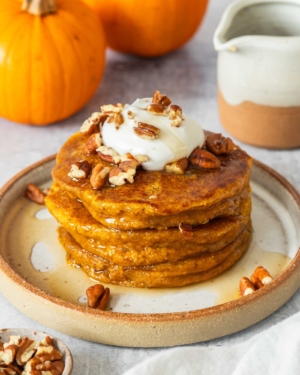 Vegan pumpkin pancakes topped with coconut yoghurt, crumbled pecans and maple syrup
