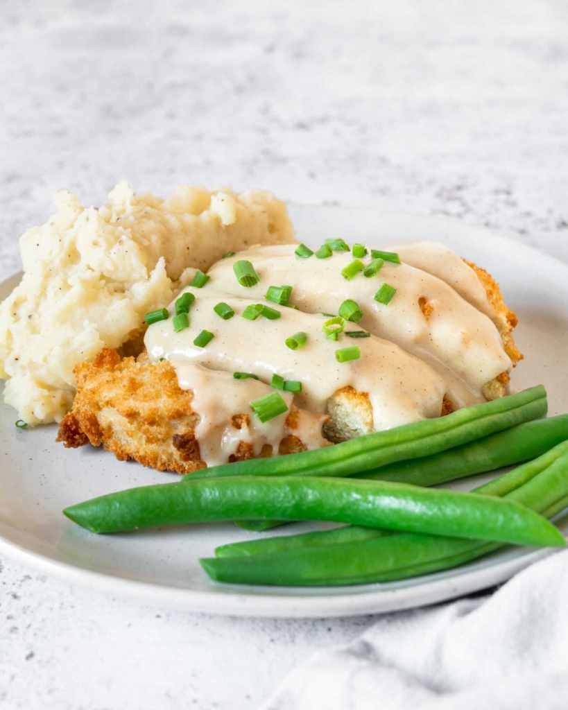 Breaded vegan chicken on a plate with green beans and white gravy