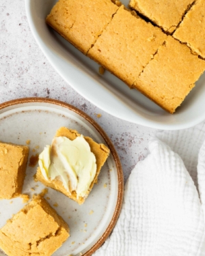 Chunky squares of golden cornbread on a plate, spread with vegan butter