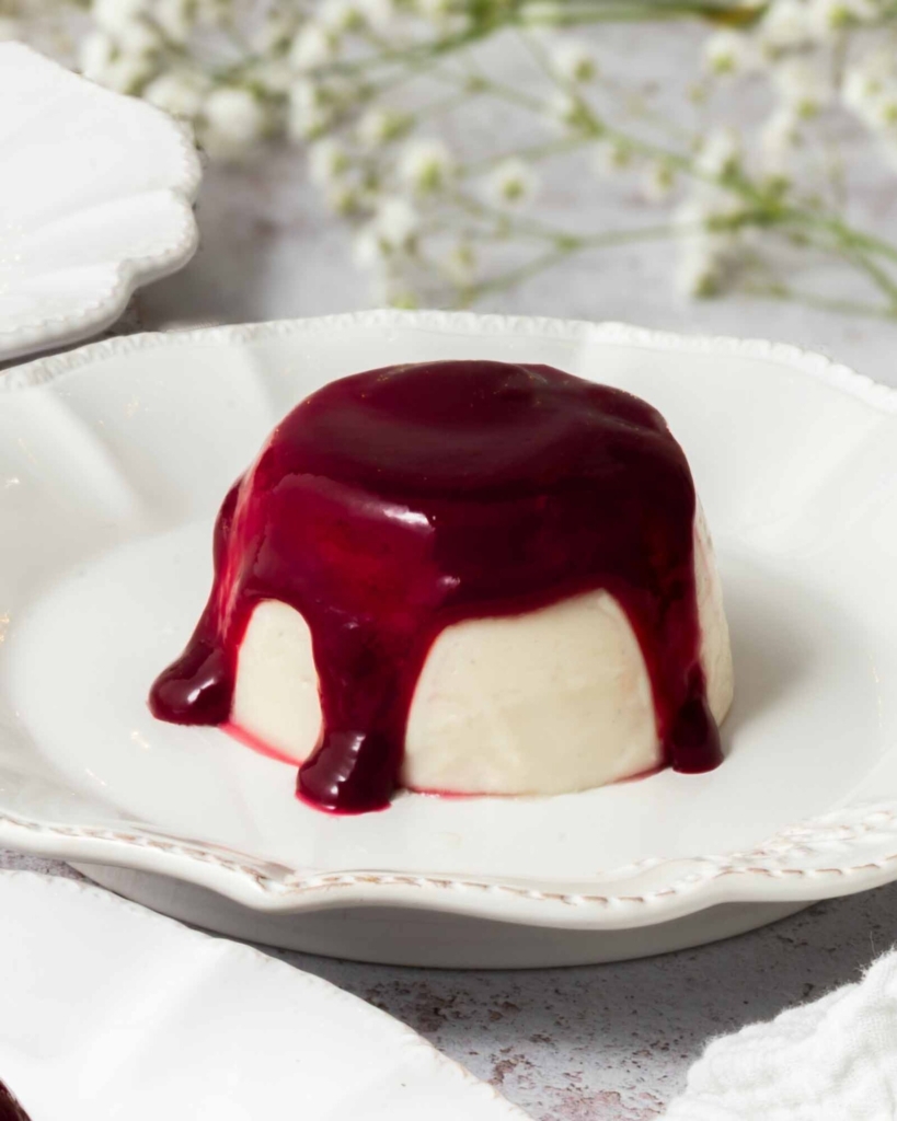 A vegan panna cotta on a white plate topped with raspberry coulis