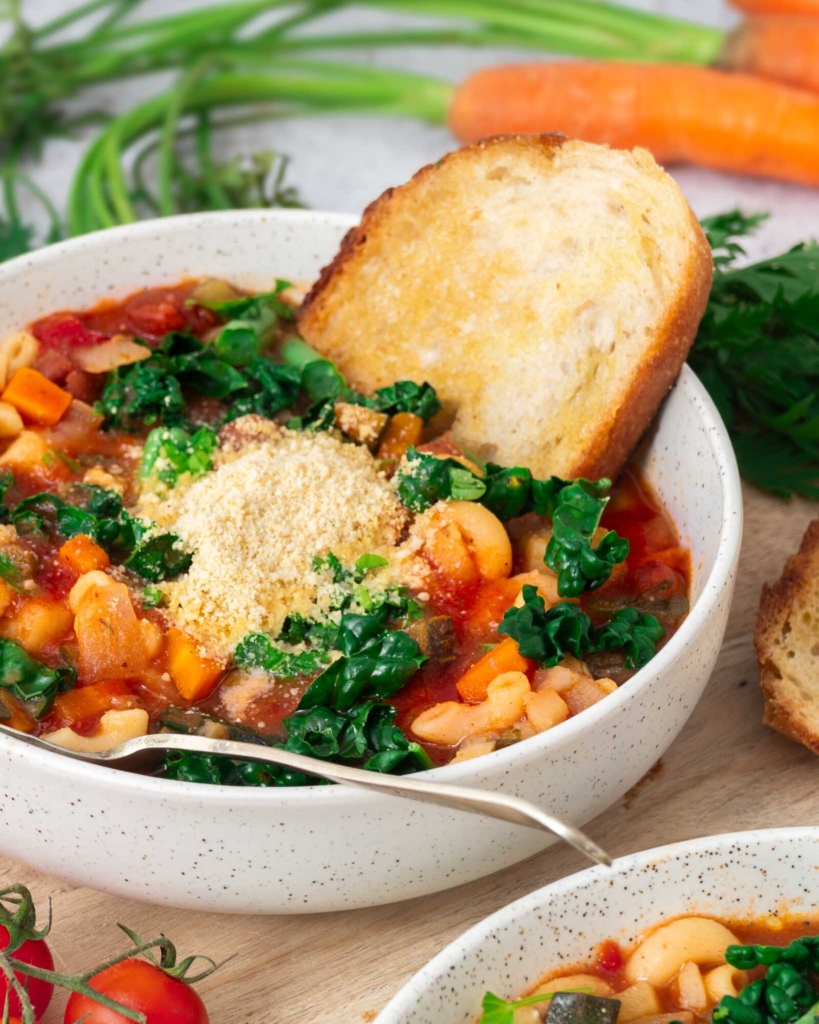 A close up image of a bowl of hearty vegetable and bean soup, topped with fresh cavolo nero and dairy free parmesan cheese