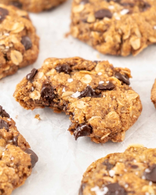 A vegan chewy oatmeal cookie with melty chocolate chips on a piece of baking paper