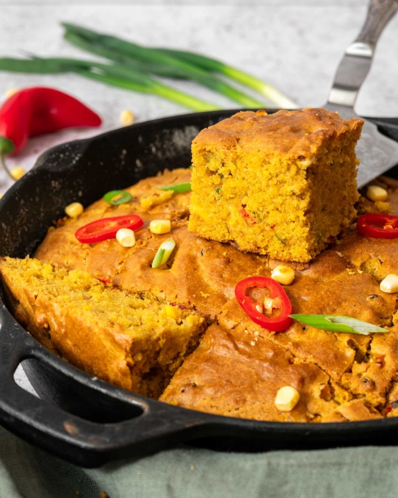 A chunky slice of Indian cornbread being lifted from a cast iron pan